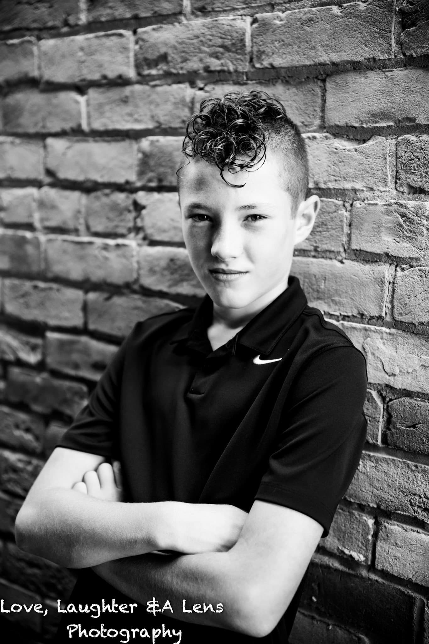 Black-and-white portrait of a child with arms crossed by a brick wall