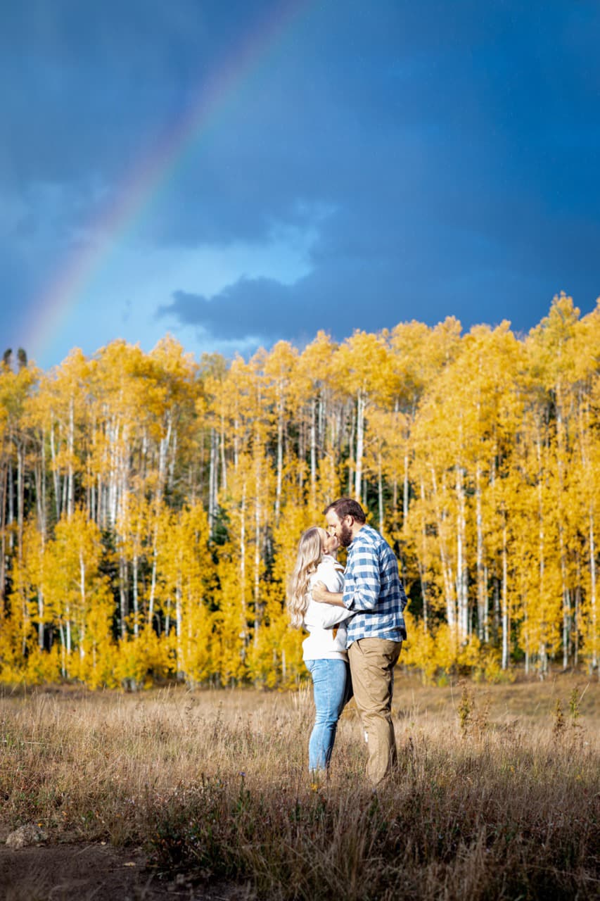 Engaged couple in golden aspens under a rainbow