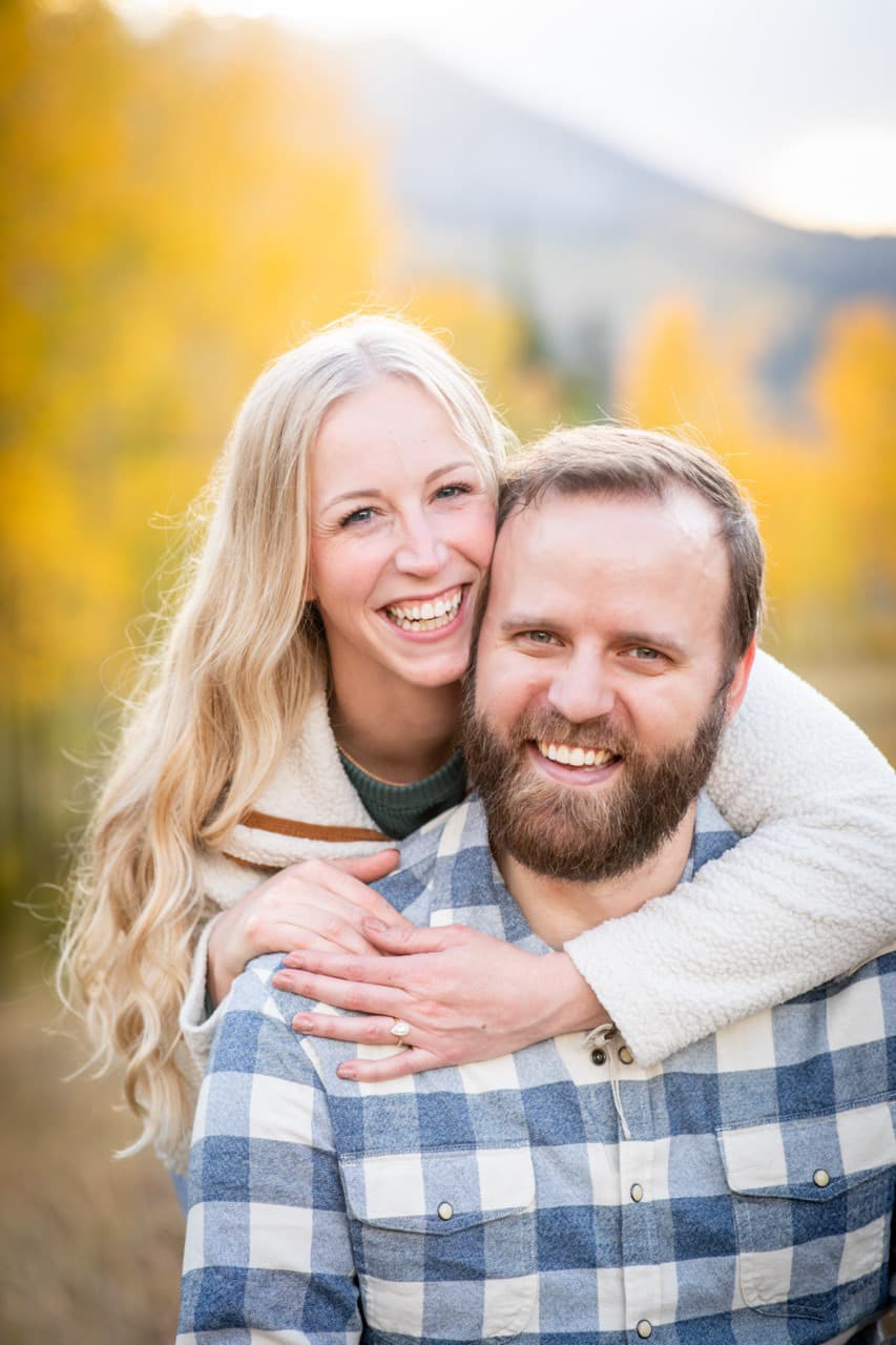 Engaged couple laughing with fall aspens behind them