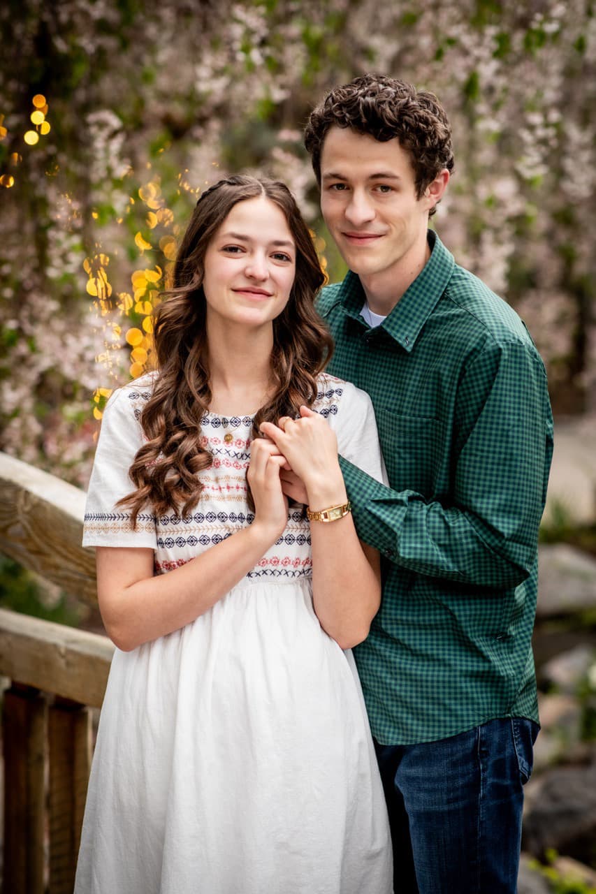 Engaged couple in front of spring blossoms by a wooden bridge