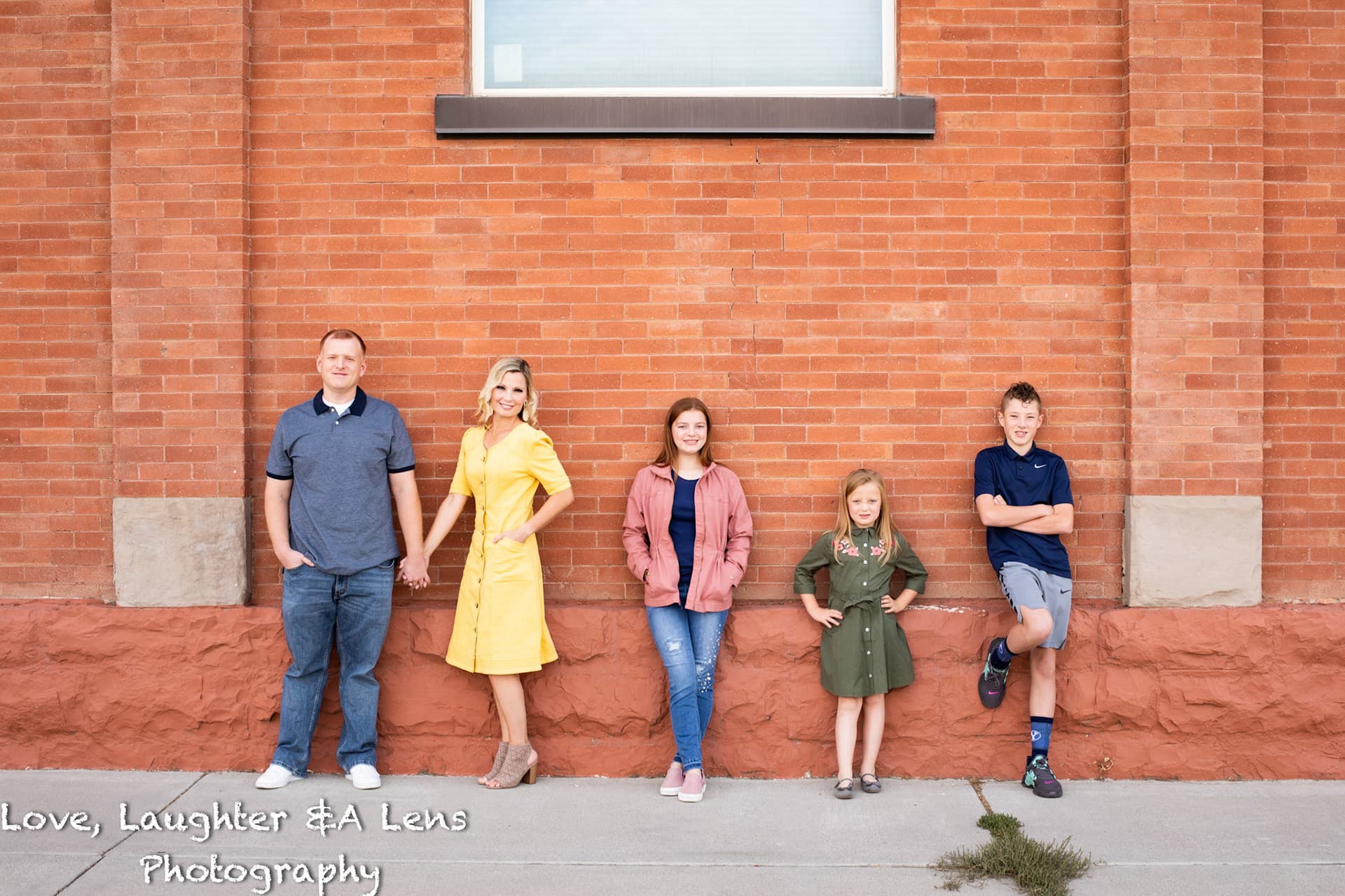 Family of five standing against a red brick wall