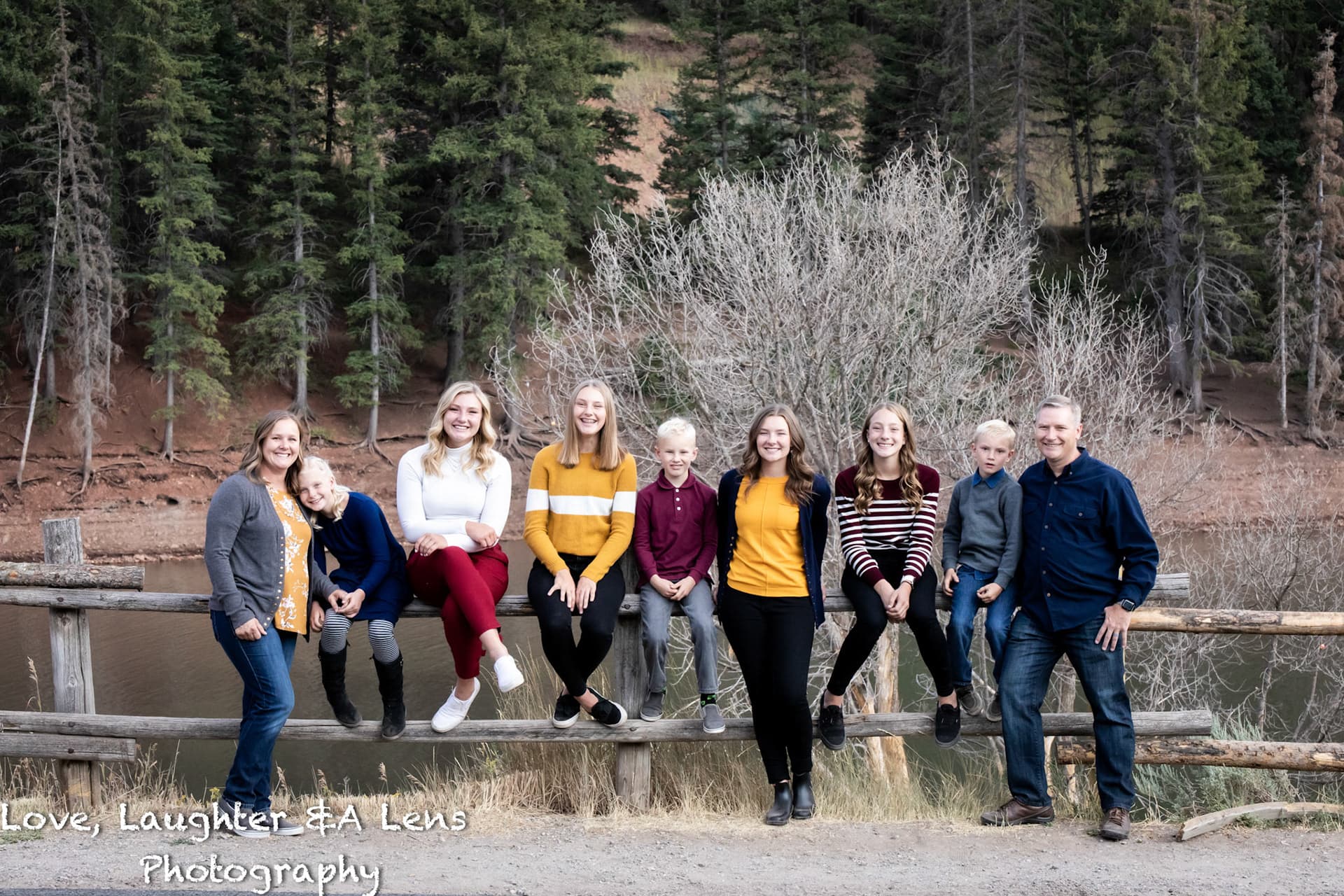 Large family sitting on a fence beside a pond and pine trees