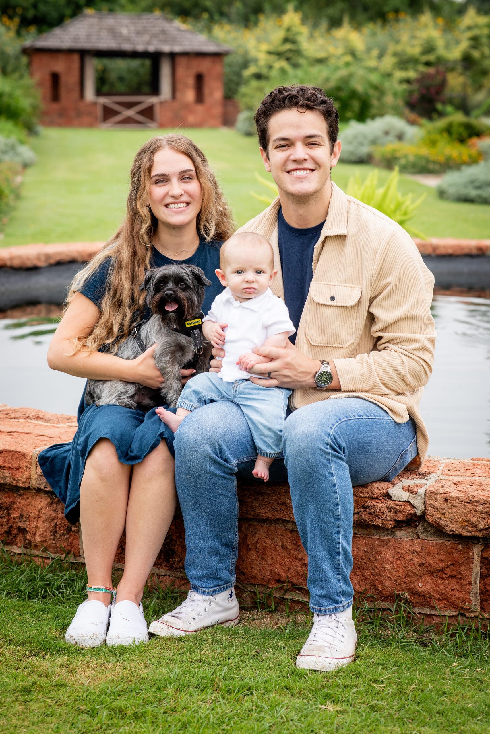 Couple with their baby and dog at the edge of a garden fountain