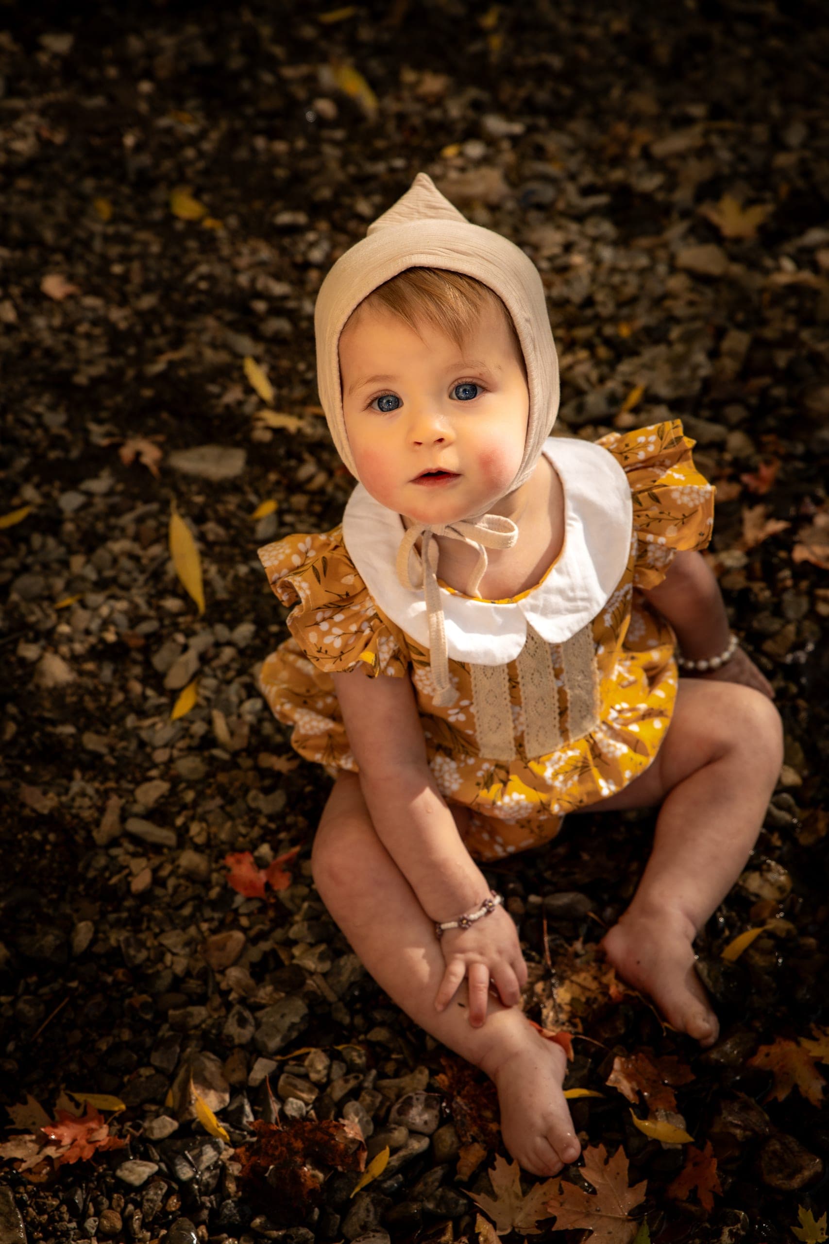 Baby in a bonnet sitting on fall leaves