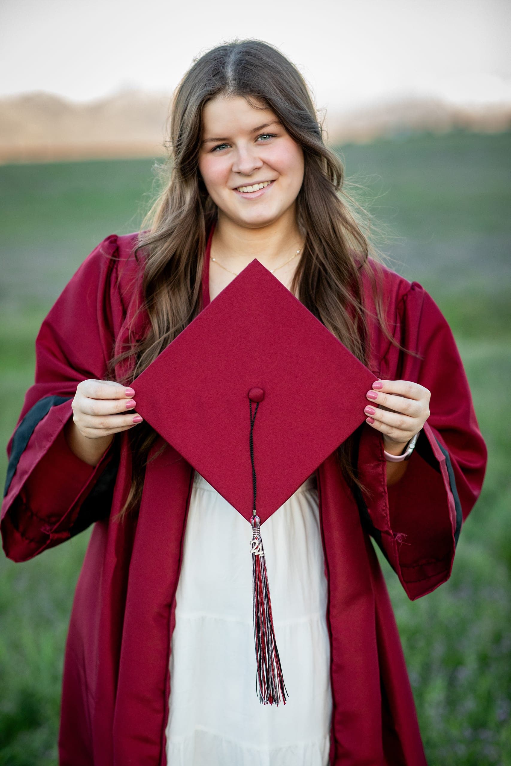 Graduate in a red gown holding up a graduation cap