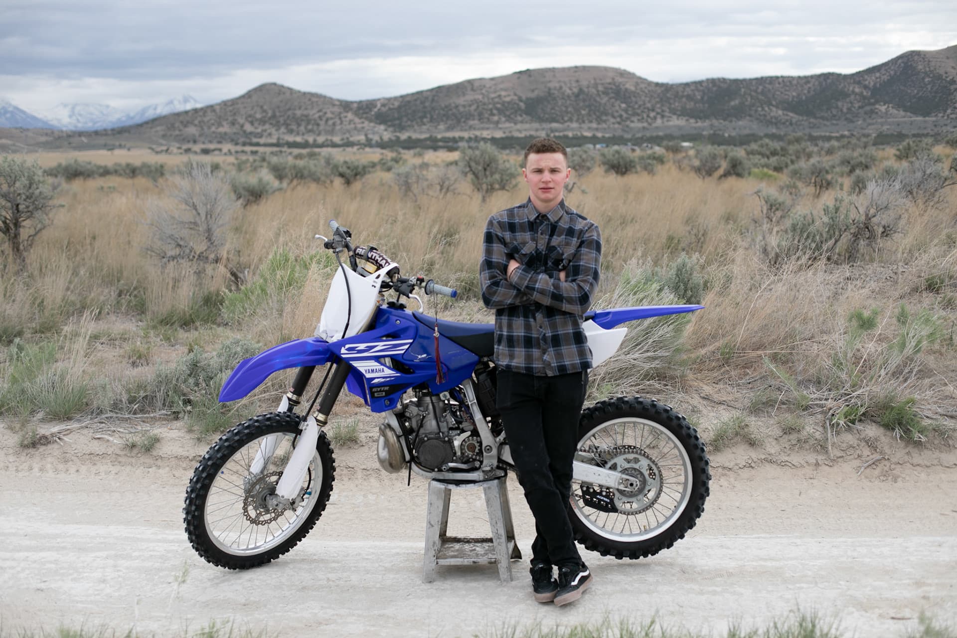 Senior standing with a blue dirt bike in the sagebrush