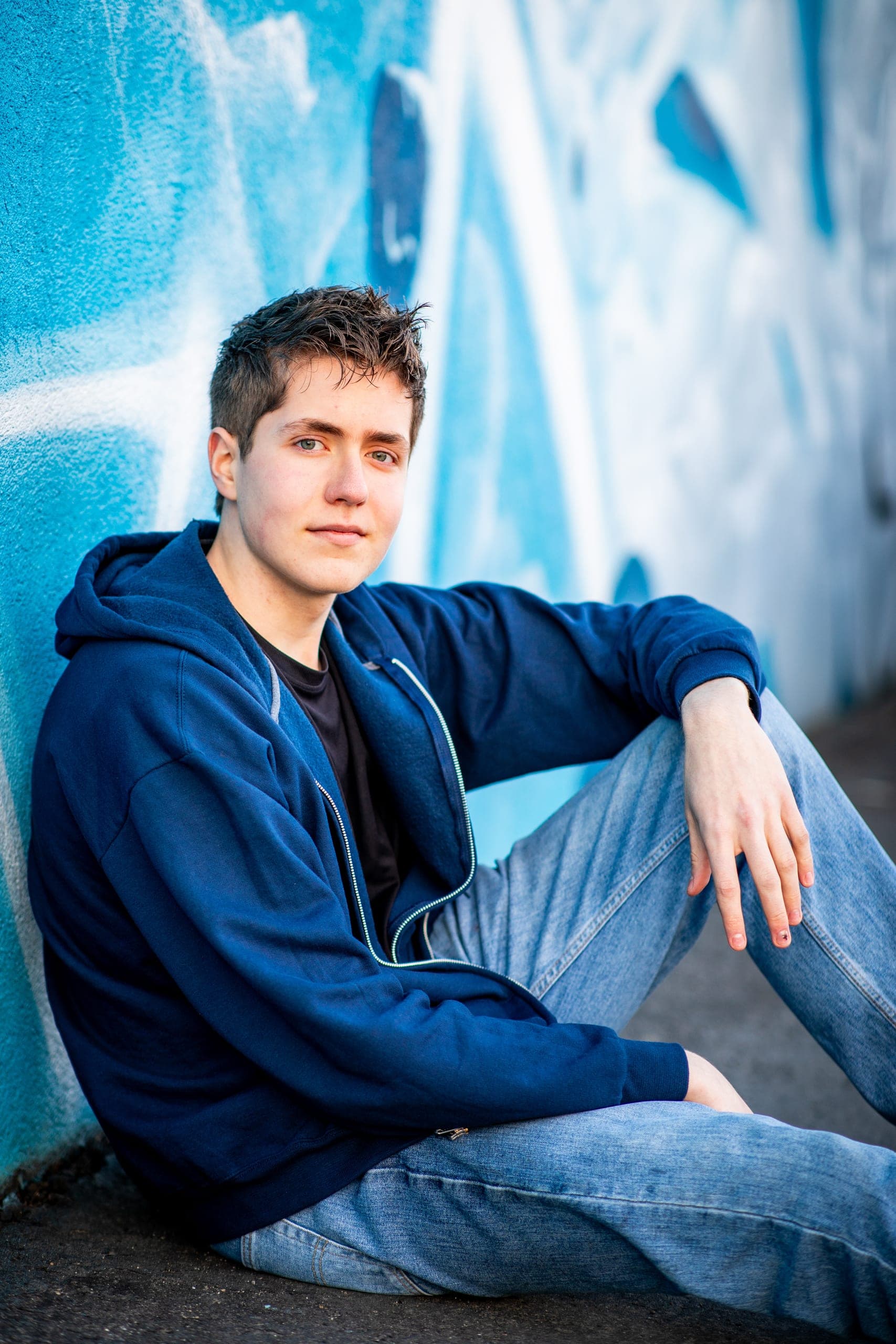 Senior sitting in front of a blue painted mural