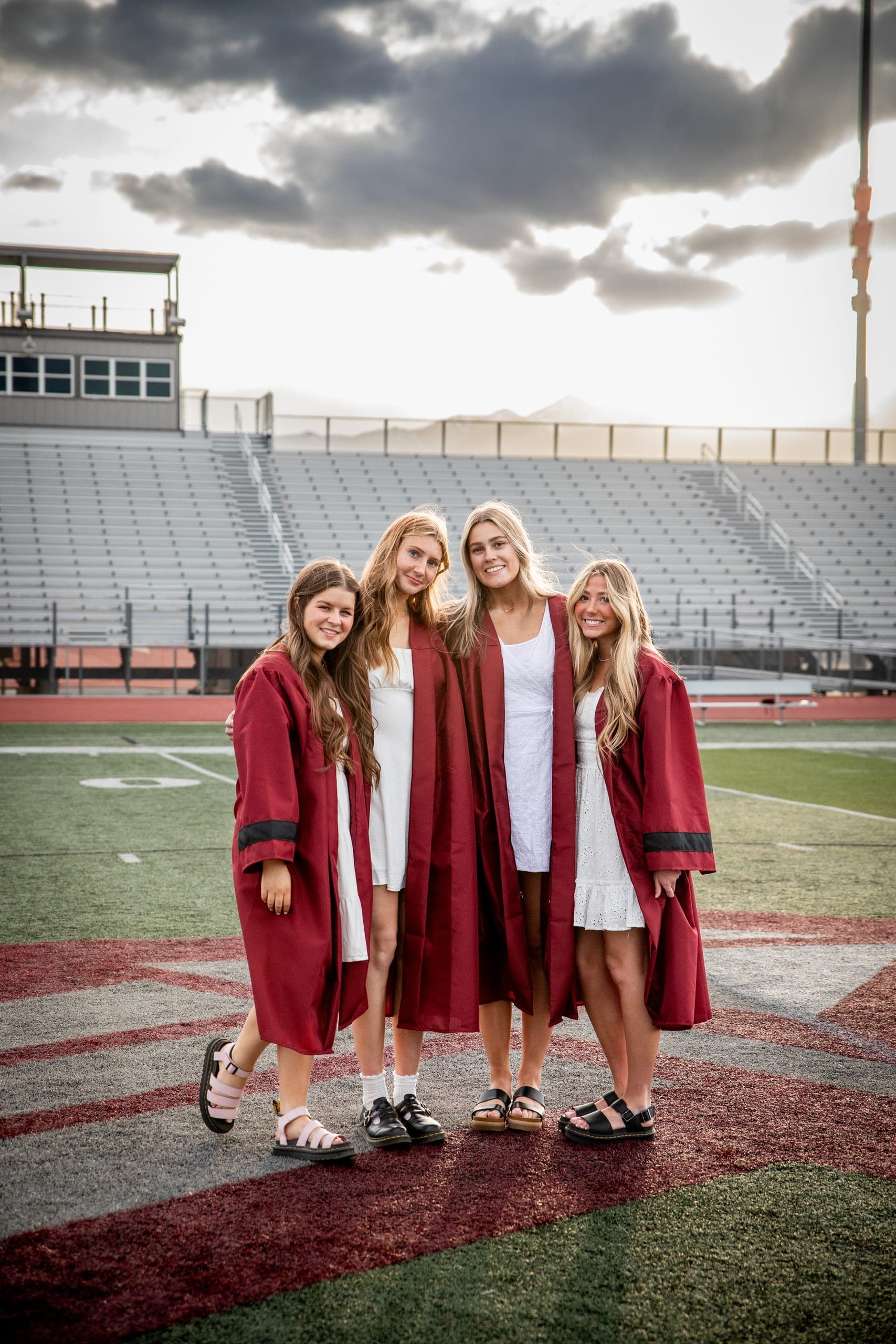 Four graduates in red gowns on a football field