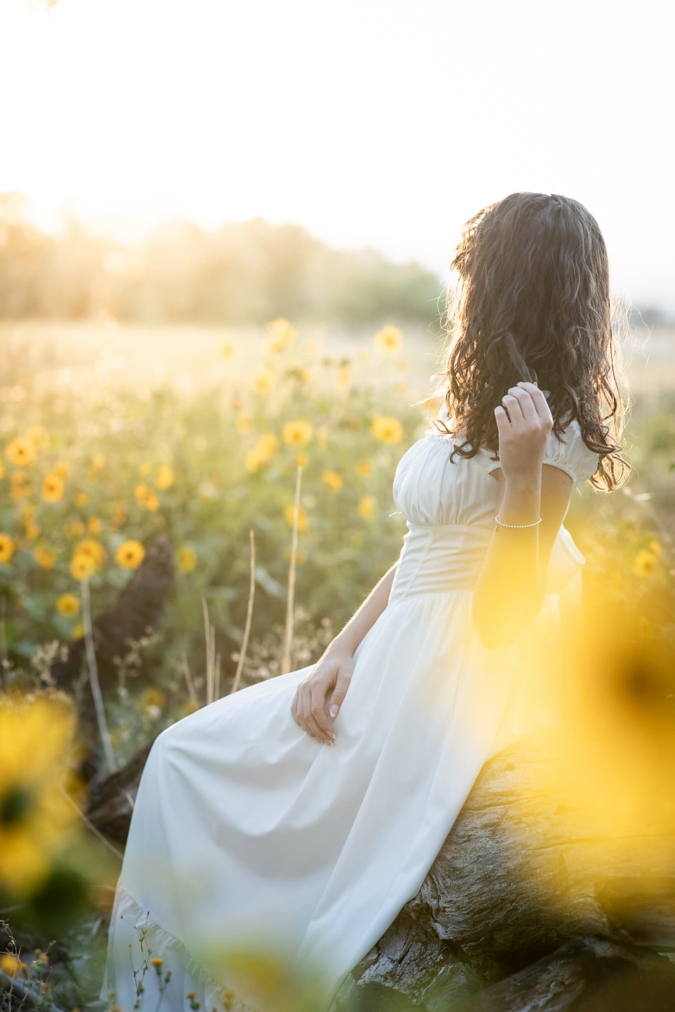 Senior in a white dress sitting among sunflowers
