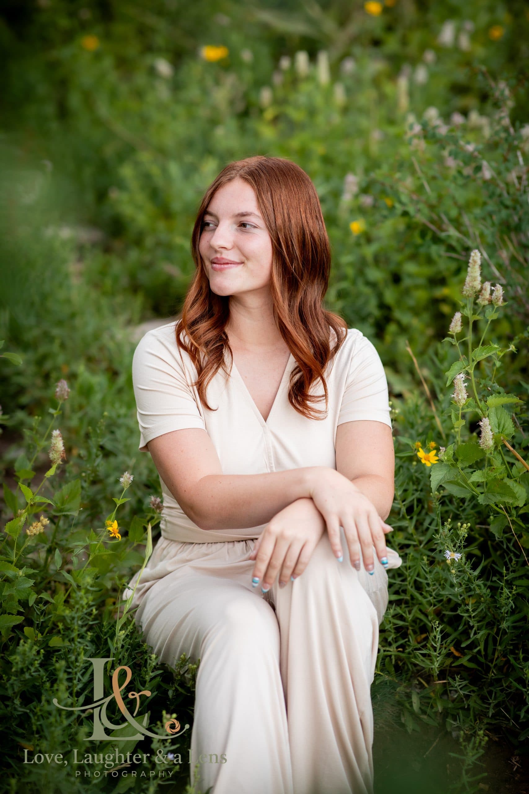 Senior in a cream outfit sitting in a green meadow