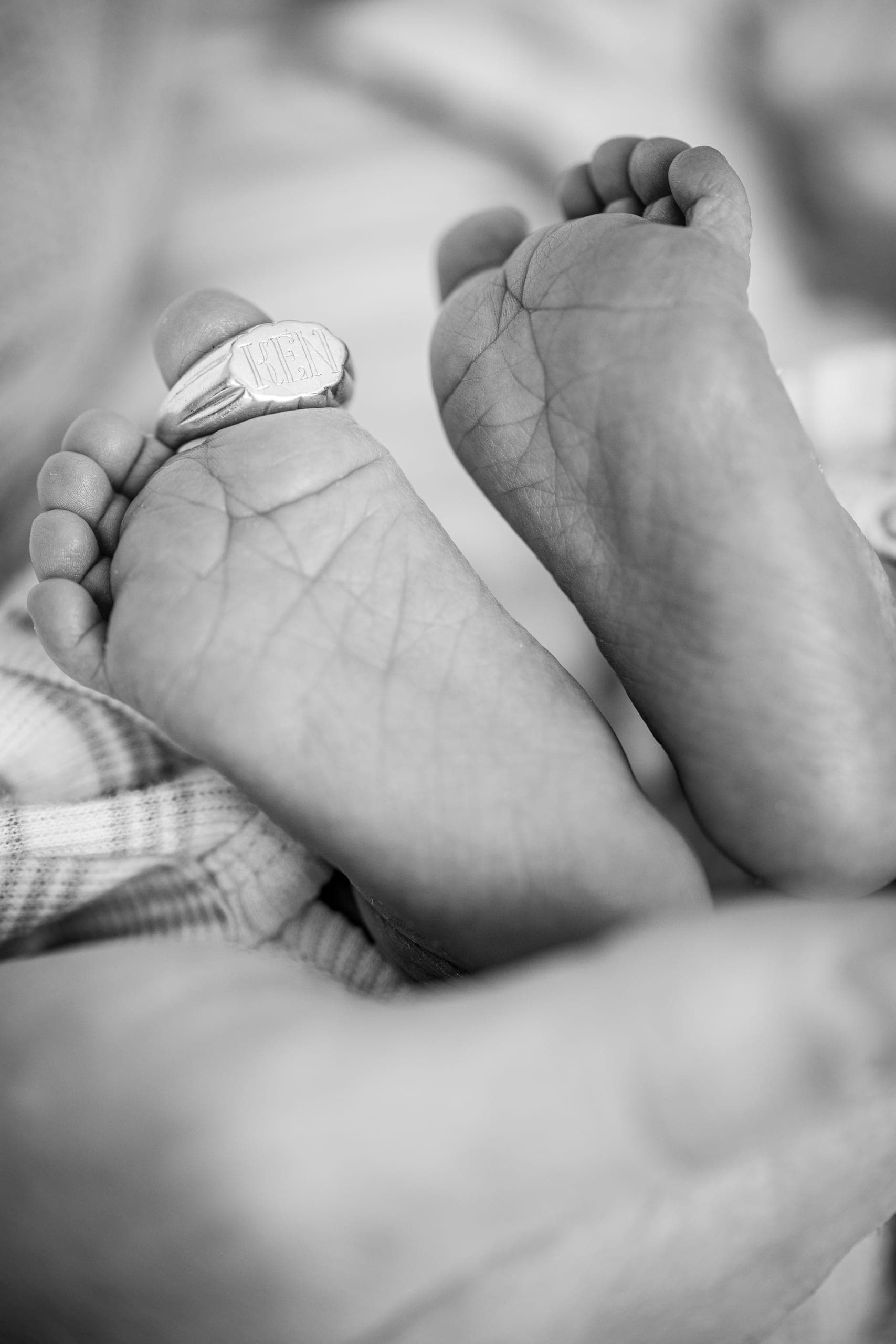 Black-and-white close-up of newborn feet holding a wedding ring