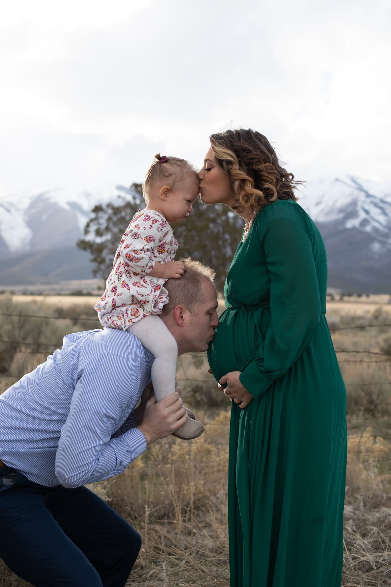 Maternity photo with a toddler on a parent's shoulders and mountains behind
