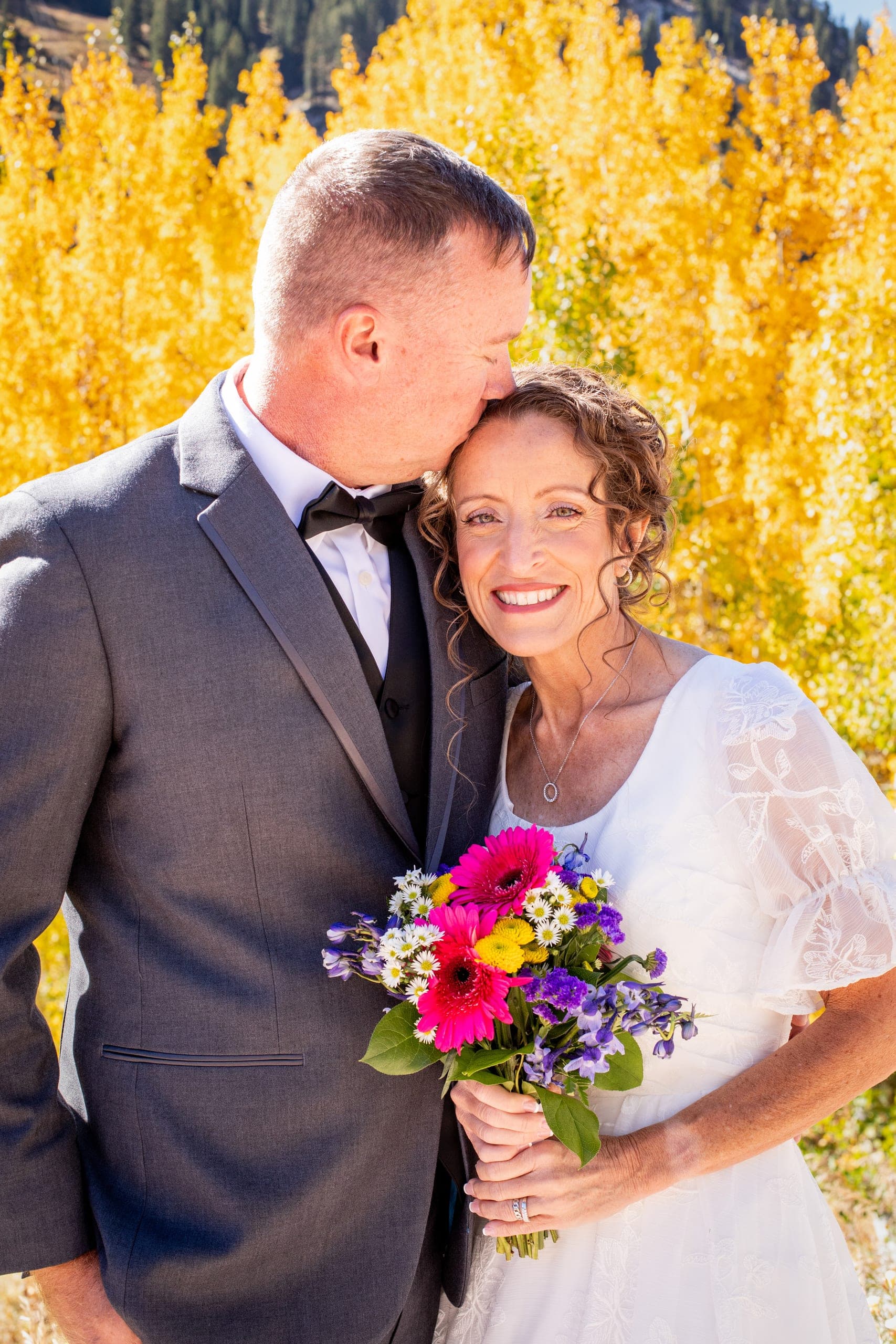 Groom kissing the bride's forehead among yellow aspens