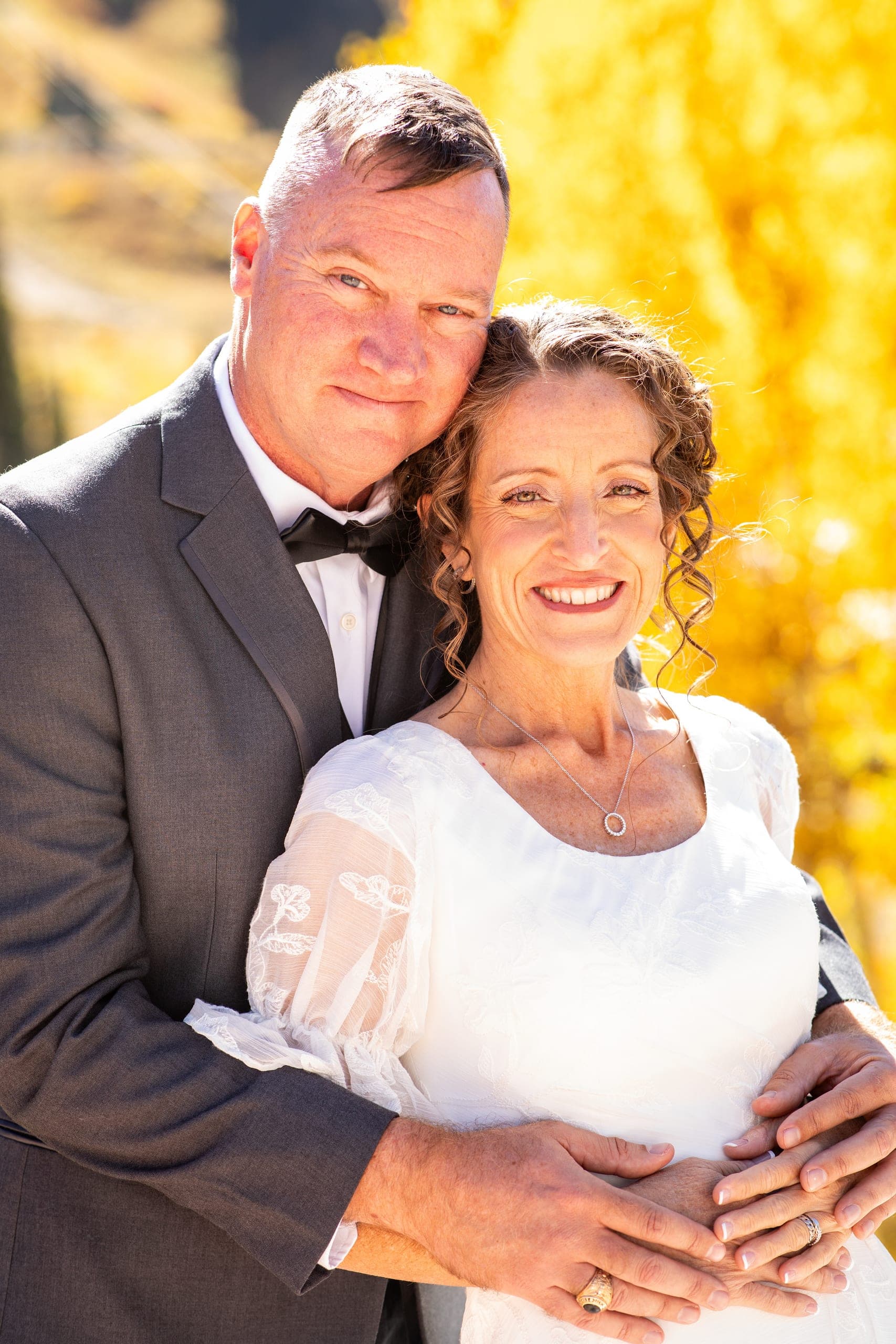Bride and groom embracing in front of yellow aspens
