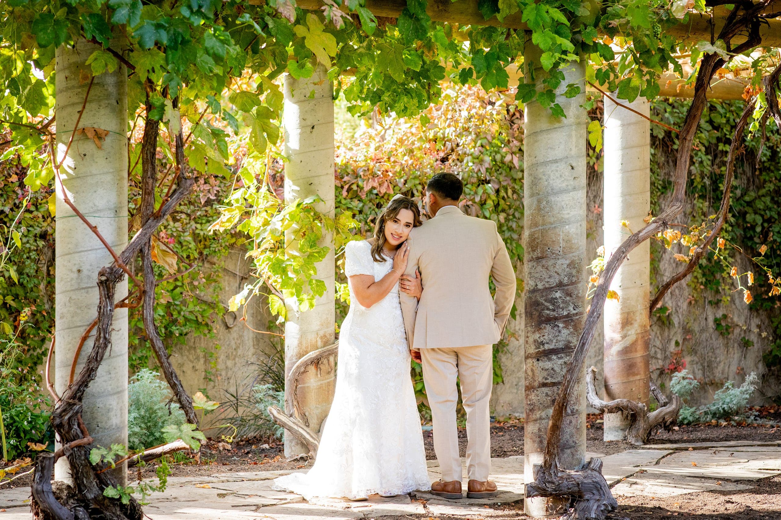 Bride and groom under a vine-covered pergola