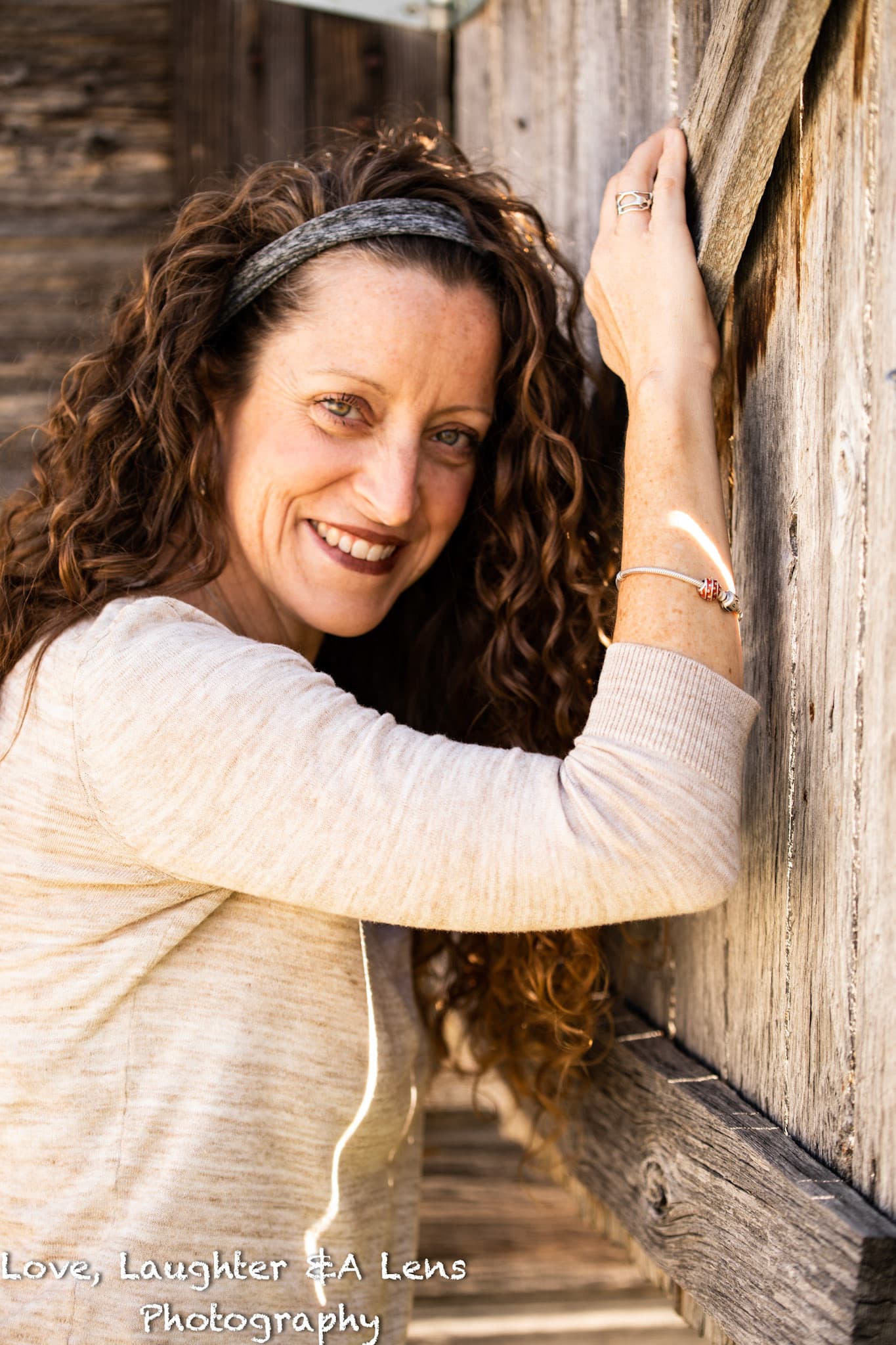 Woman with curly hair smiling against a weathered wood wall
