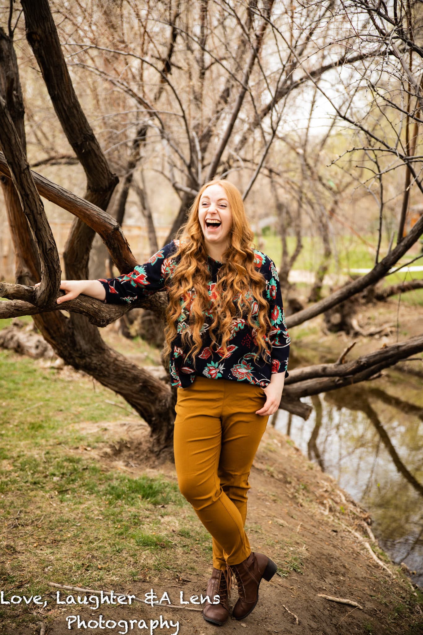 Woman with red hair laughing in a tree beside a creek